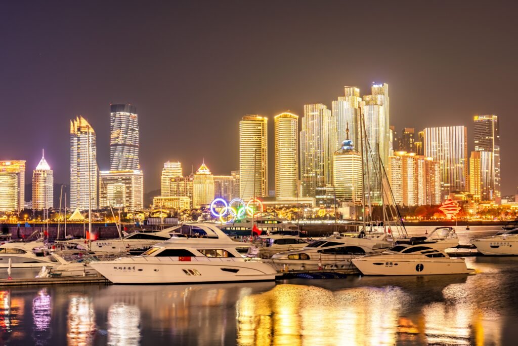 Qingdao's marina with motor yachts and glowing skyscrapers at night, showcasing its vibrant cityscape.