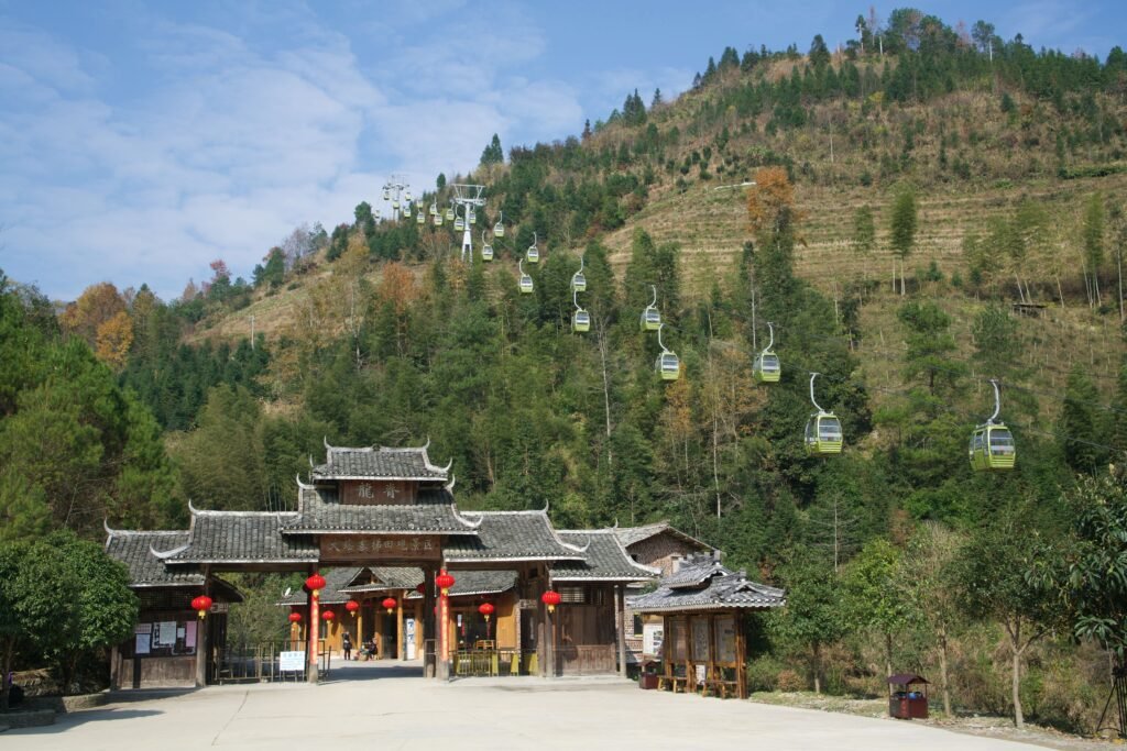 A traditional temple entrance with cable cars ascending a lush mountain landscape.