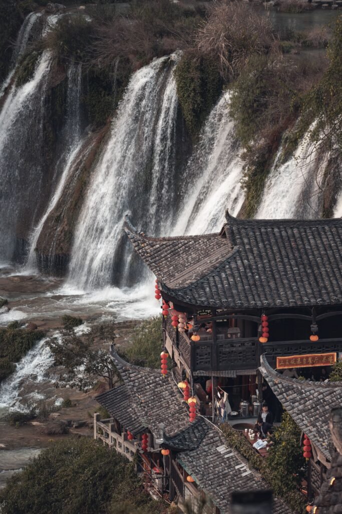 Traditional architecture with cascading waterfalls in Xiangxi, Hunan, China, creates a picturesque rural landscape.
