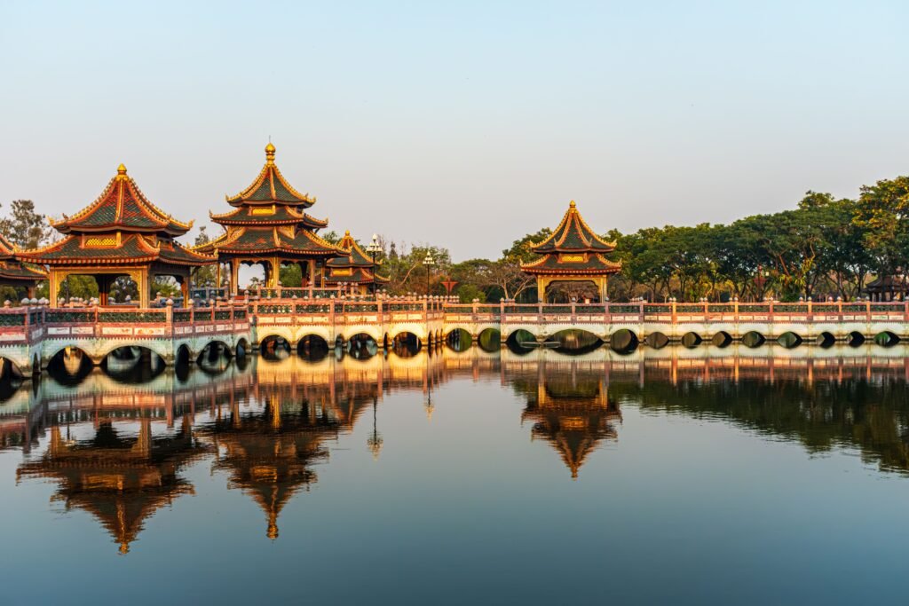 Stunning reflection of Thai architecture on a tranquil lake in Bangkok at sunset.