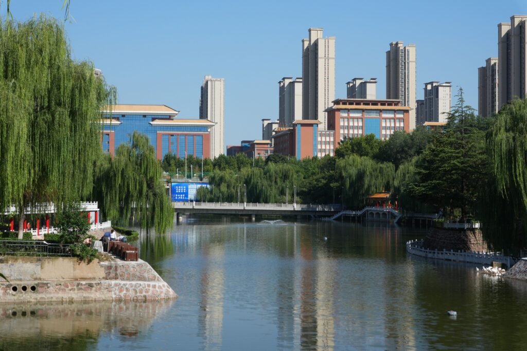 Skyscrapers reflecting on a serene river flanked by lush greenery and urban architecture.