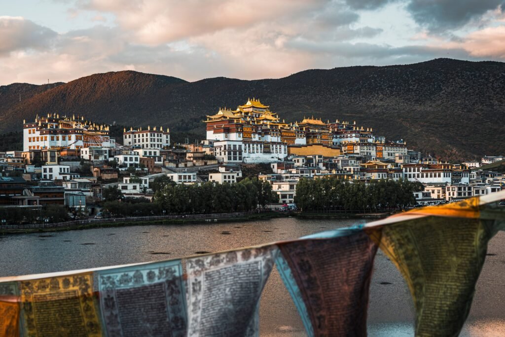 Scenic view of Songzanlin Monastery at sunset in Yunnan, China, with prayer flags in foreground.